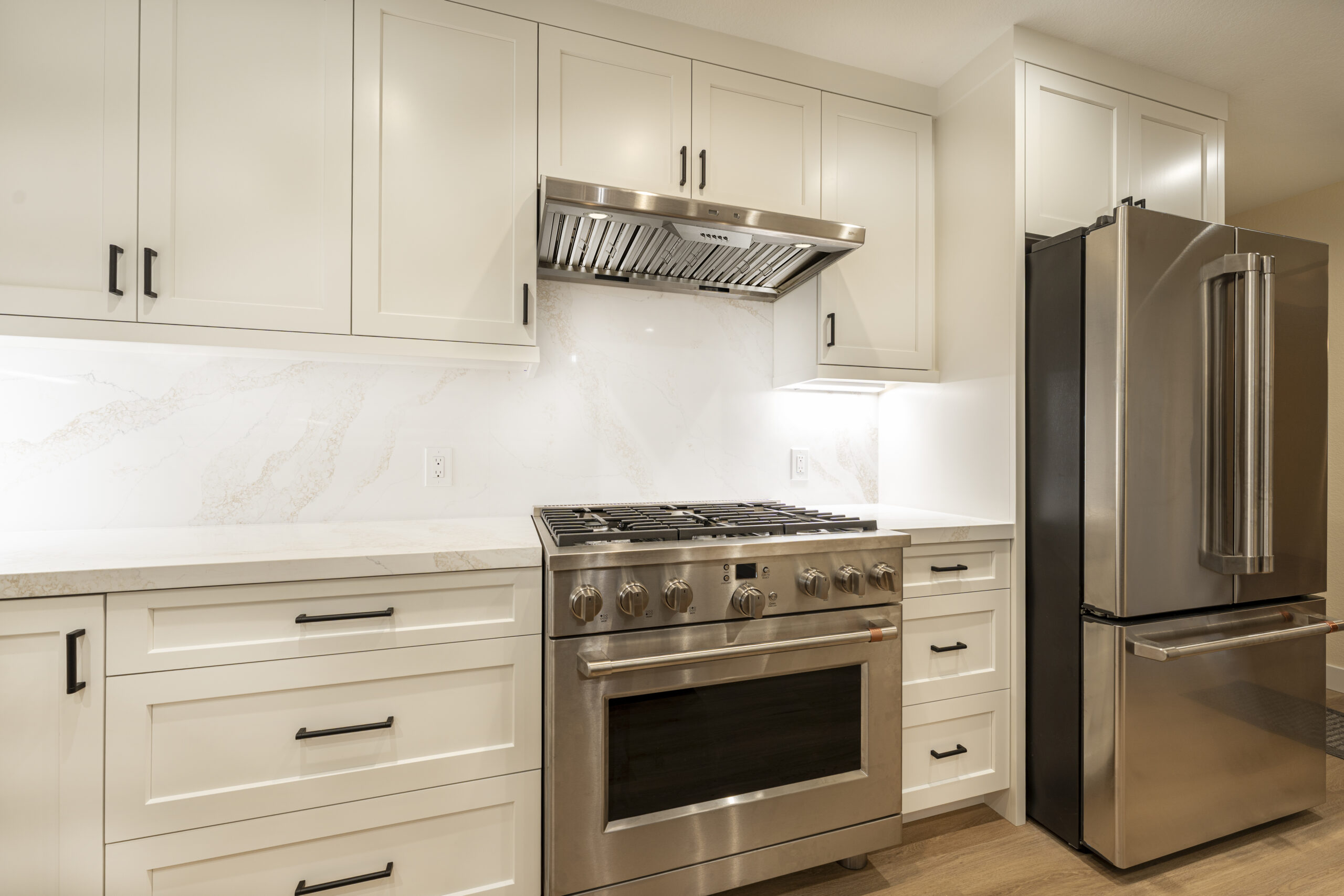 Stainless steel stove and hood with white cabinets and under cabinet lighting.